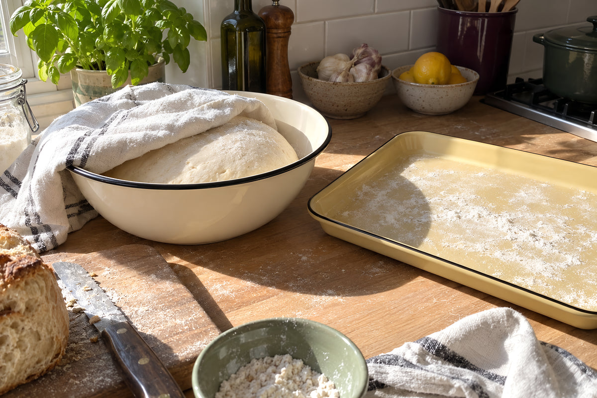 Dough proving under a tea towel in a cream KILN Bowl on a sunny worktop, the mustard KILN Tray floured and waiting beside it. Daytime, hard sun, no candles lit.